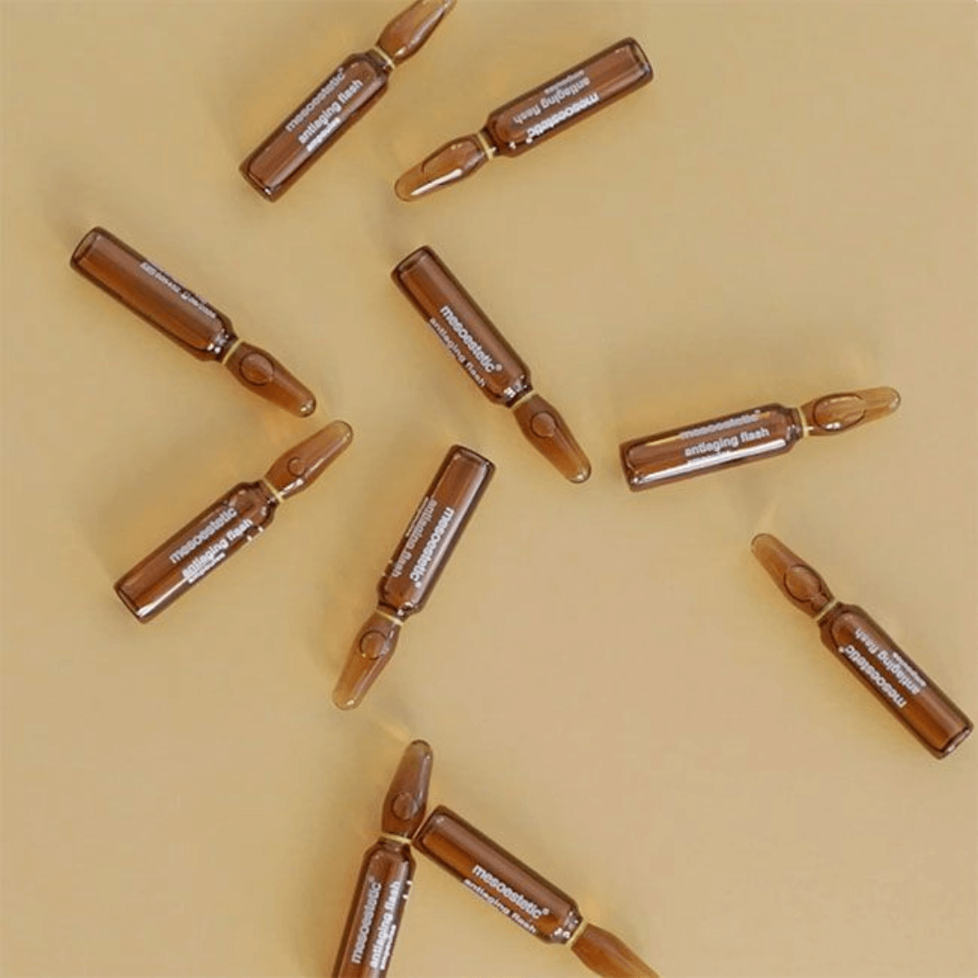 Scattered Mesoestetic antiaging ampoules on yellow, instant lifting, suitable for all skin types.