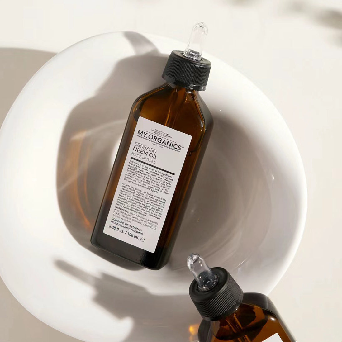 Two bottles of My Organics Neem Oil in a white bowl, showcasing the natural oil's packaging and uses.