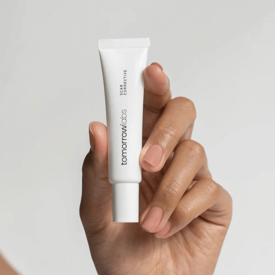 A person holding a tube of Tomorrowlabs Scar Corrective, showing a close-up of the hand and the product.